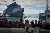 Photograph of a mother holding her child and a rainbow umbrella at a shipping port.