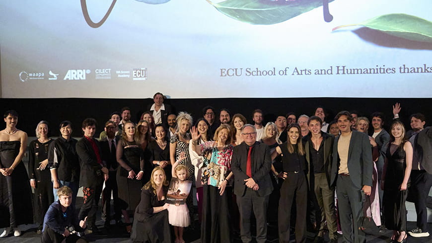 Large group of people gathered for a photo with cinema screen in background with elements ECU School of Arts and Humanities.