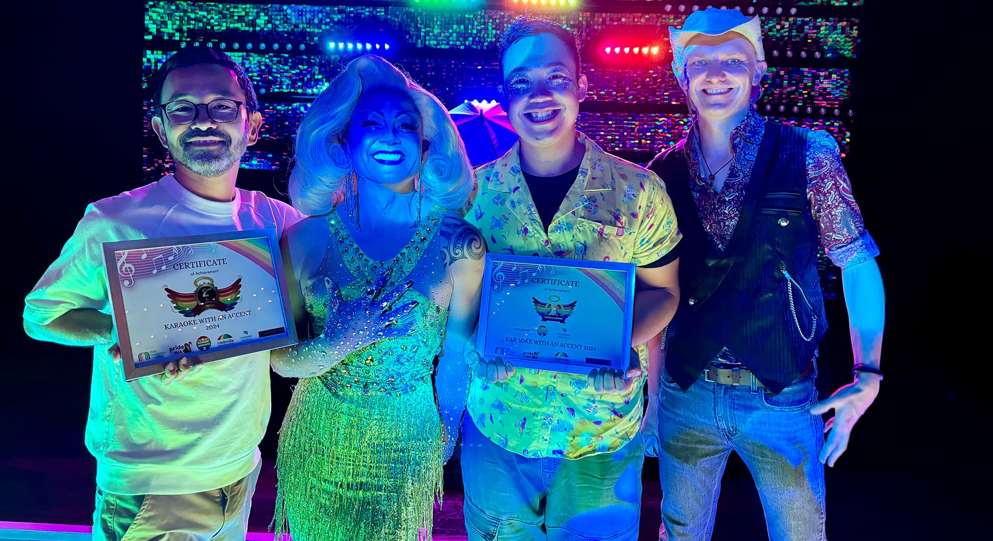 Four smiling people standing side by side in nightclub lighting two holding certificates