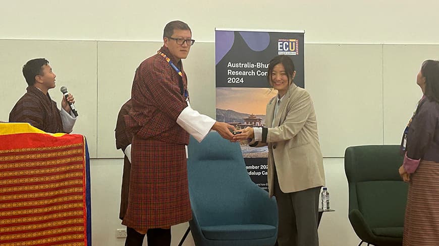 A man dressed in Bhutanese clothing shakes hands with a student at a conference.