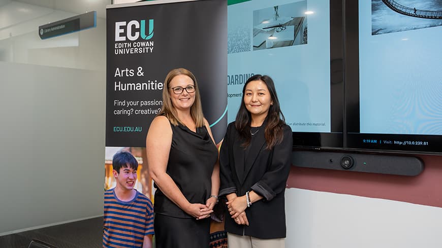 Two women stand next to each other in front of a pull-up banner and presentation at a workshop.