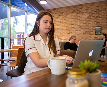 A nursing student at ECU South West campus looks up literature using a laptop in a relaxed cafe setting.