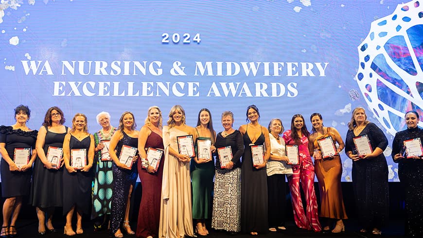 Winners stand on stage holding their framed awards. The words 2024 WA Nursing and Midwifery Awards appears at the back.