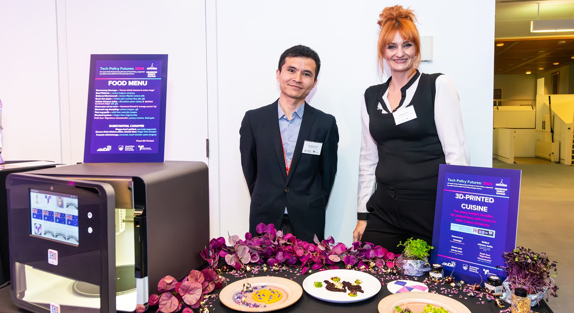 Dr Liezhou Zhong and Amanda Orchard at the Tech Policy Futures event standing behind a table with 3D printed foods, decorative flowers and a 3D printer.