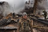 Soldier standing amongst rubble of a burning building.