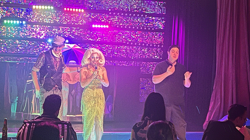 Three people standing on a stage in a nightclub with pink and purple lights