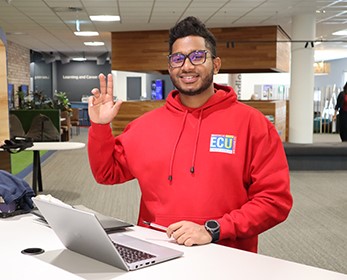 Library Peer Assistant smiling at the front desk, ready to help students.