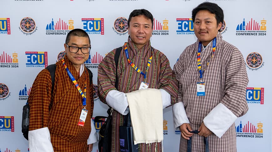 Three people in Bhutanese dress in front media wall with ECU logo