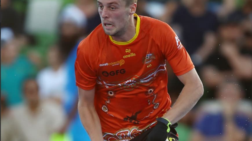 torso of field hockey sportsman in red shirt with blurred crowd in background