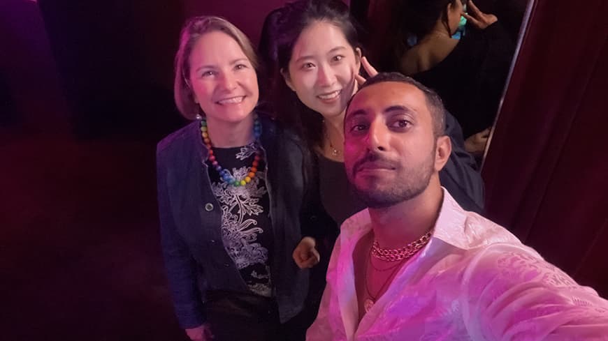 Three people in a selfie smiling up at the camera, guy in foreground holding camera in white shirt