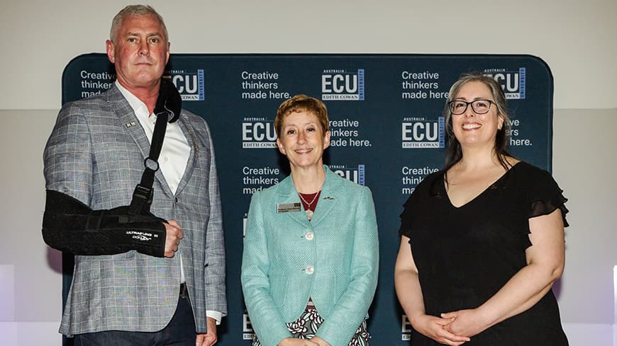 Three people in front of navy blue backdrop with ECU logos, on the left a tall man with his arm in a sling, centre lady in aqua jacket and lady in lady on the right