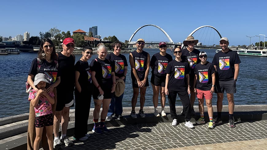 11 people and a child standing on paving edge of river in matching ECU pride t-shirts