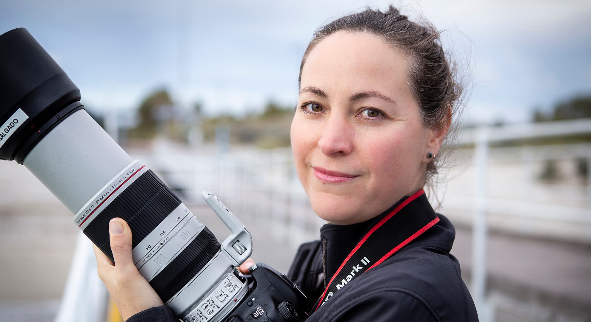 Professor Chandra Salgado Kent has her hair tied back, wears a dark grey jacket and holds a DSLR camera with a telephoto lens.