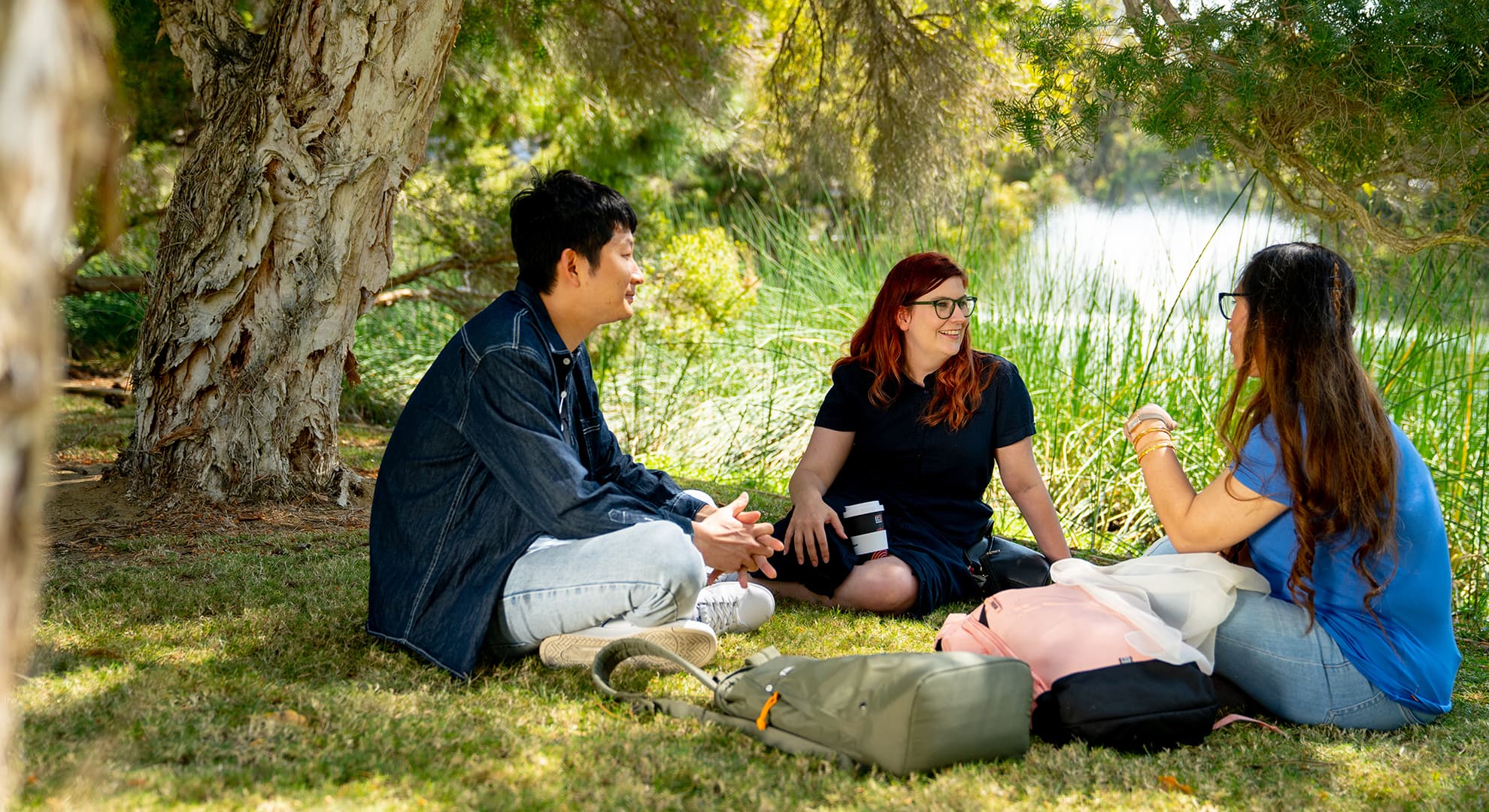 Three ECU students chat alongside the lake on Joondalup Campus.