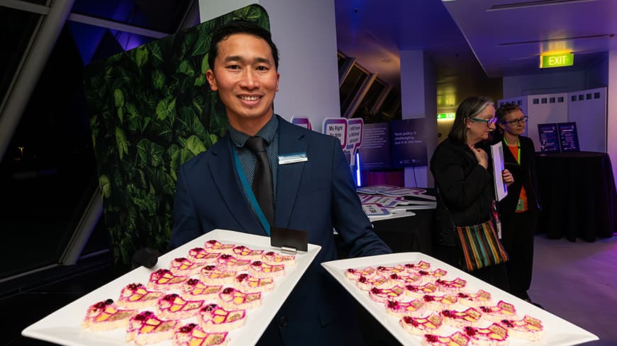 A waiter wearing a suit holding out 3D printed canapes at a tech event.