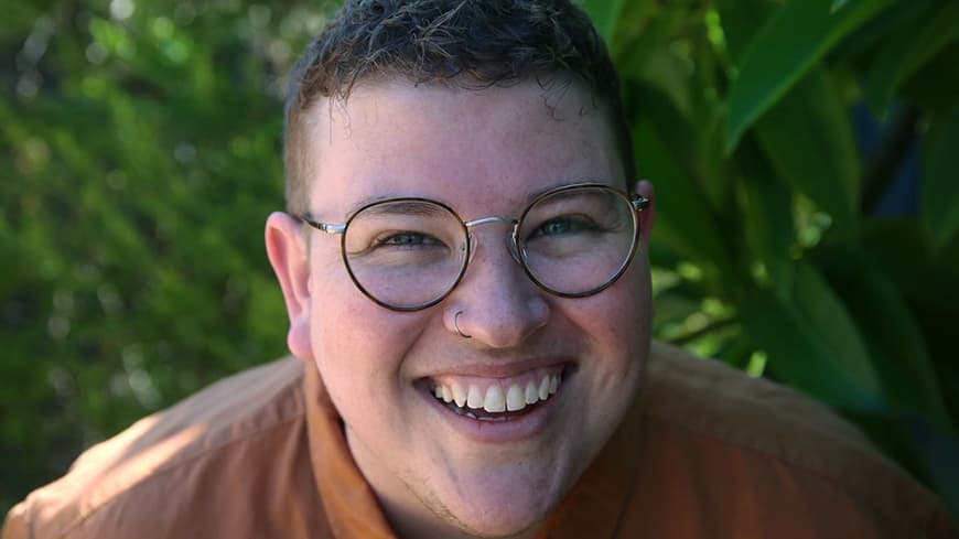 Head and shoulders close up of smiling person with very short hair and glasses