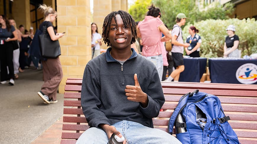 Young person smiling and giving the thumbs up on a bench