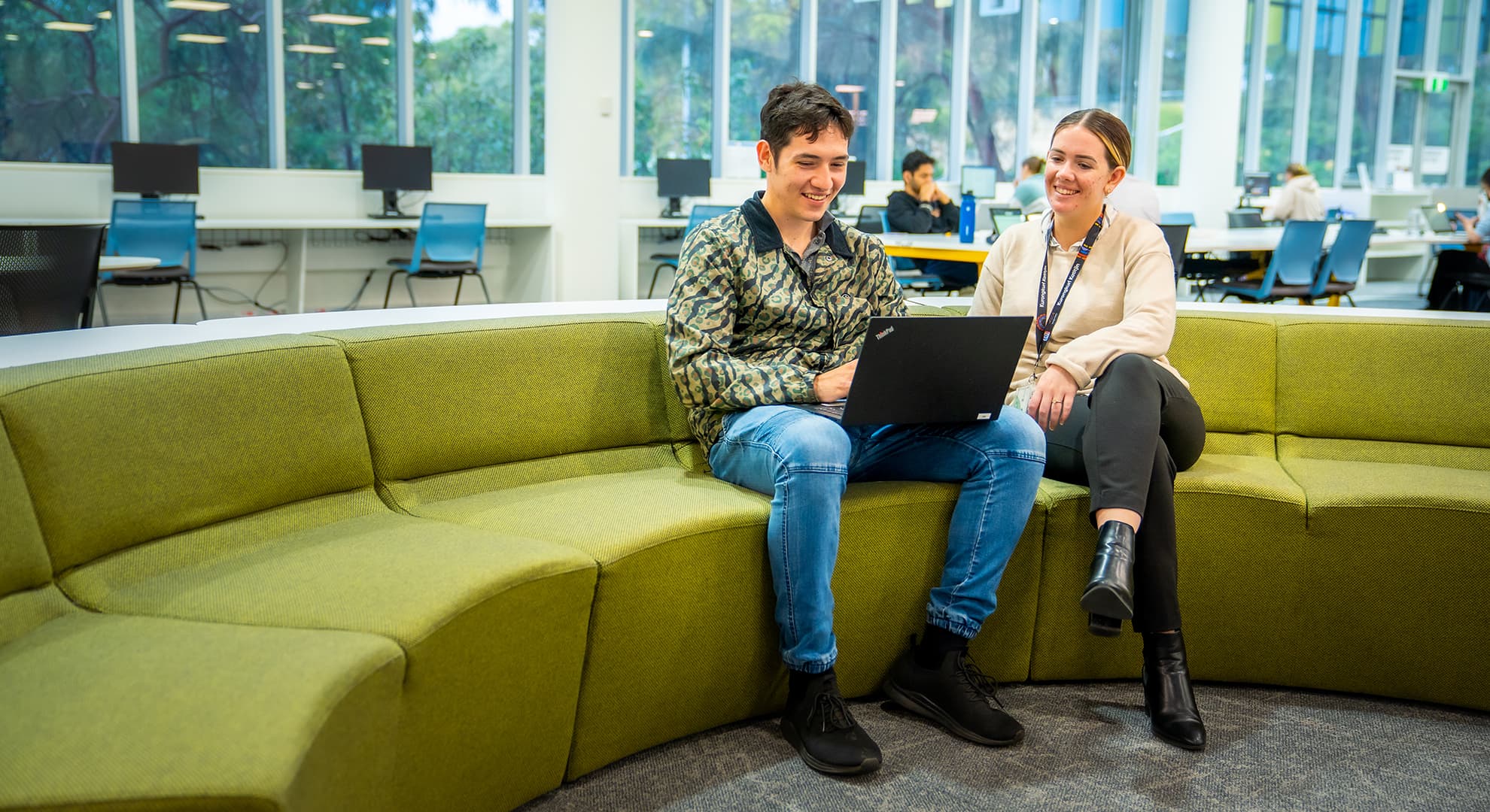 Two students sitting on couch in Library looking at a laptop and talking