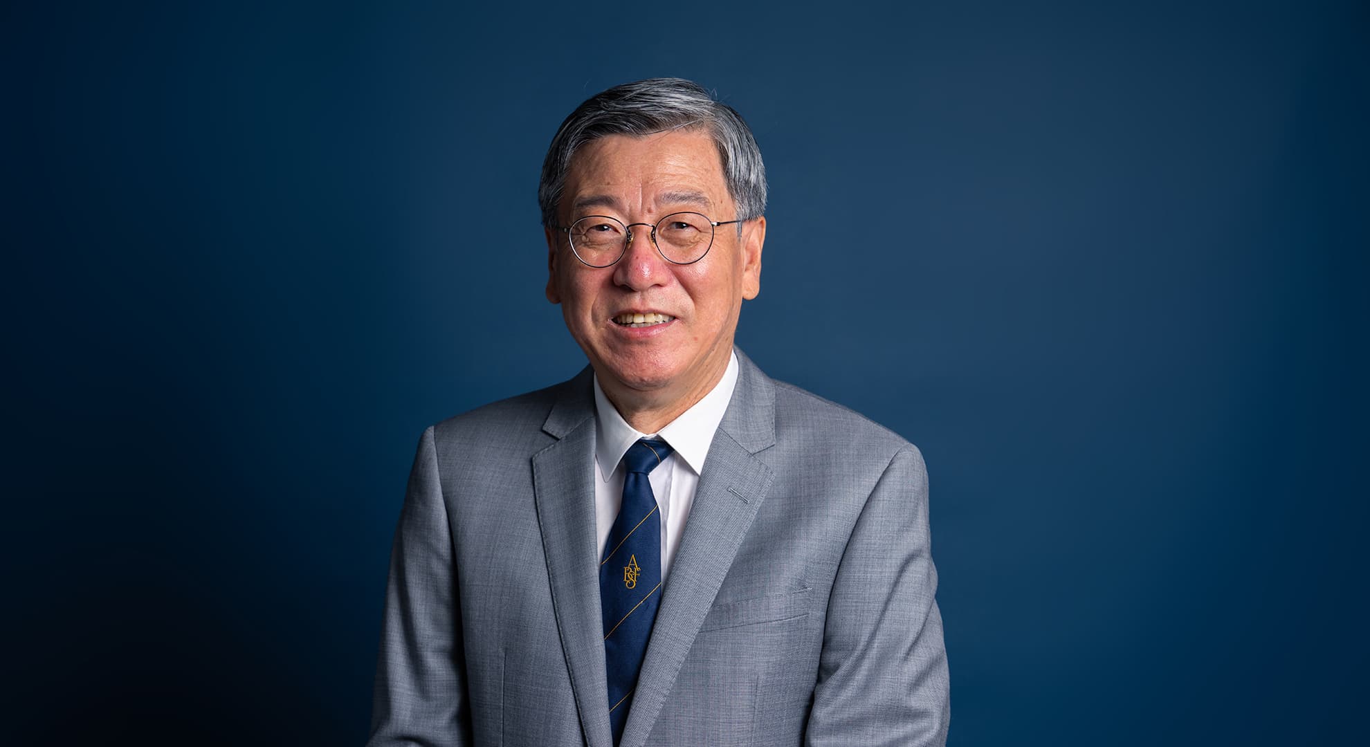 Professor Wei Wang wears a grey suit, blue tie, and silver-framed glasses.