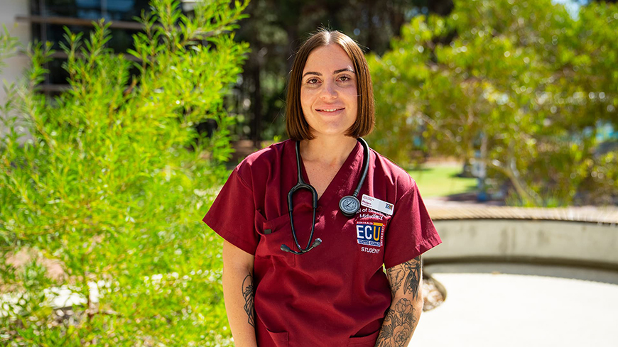 Nursing student Rhiarn Snowden wears red nursing scrubs with a stethoscope around her neck.