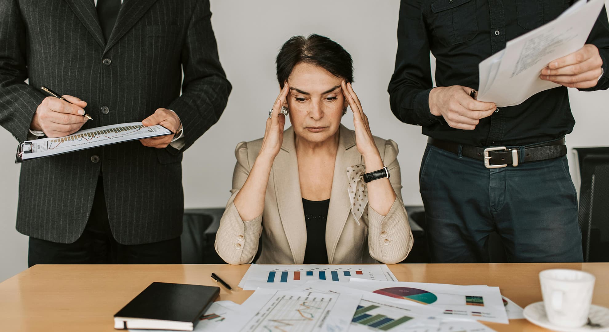 Woman holding head while sitting between two standing men.