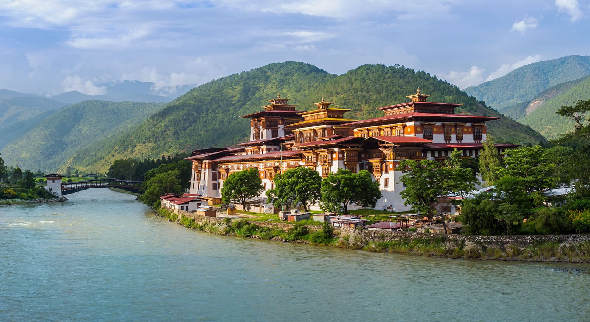 A Buthanese castle next to the Bhutan Punakha Dzong River with green mountains in the background.