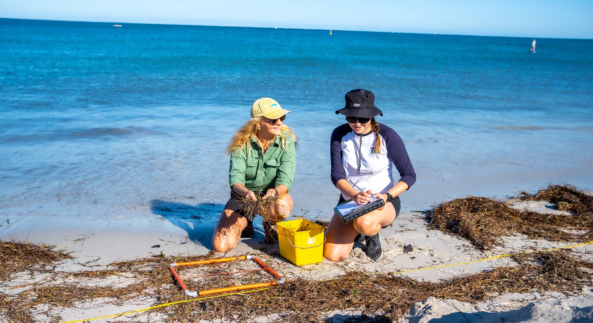 Two ECU science students crouch on the sand collecting samples from the beach for their research.