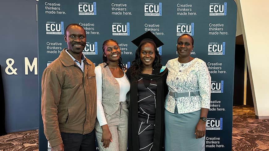 Purity Osiako is dressed in her graduation regalia, gown and cap and stands with her family.