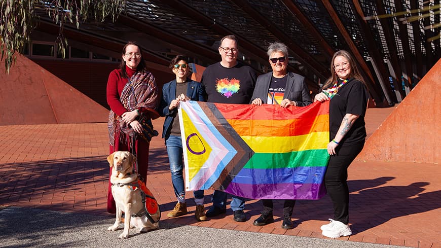 Five people and a dog standing holding pride flag.