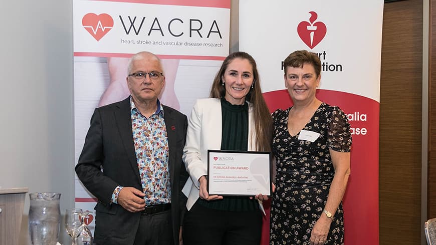 Dr Simone Radavelli-Bagatini holds her framed award with two academics, WACRA pull-up banners are placed behind them.