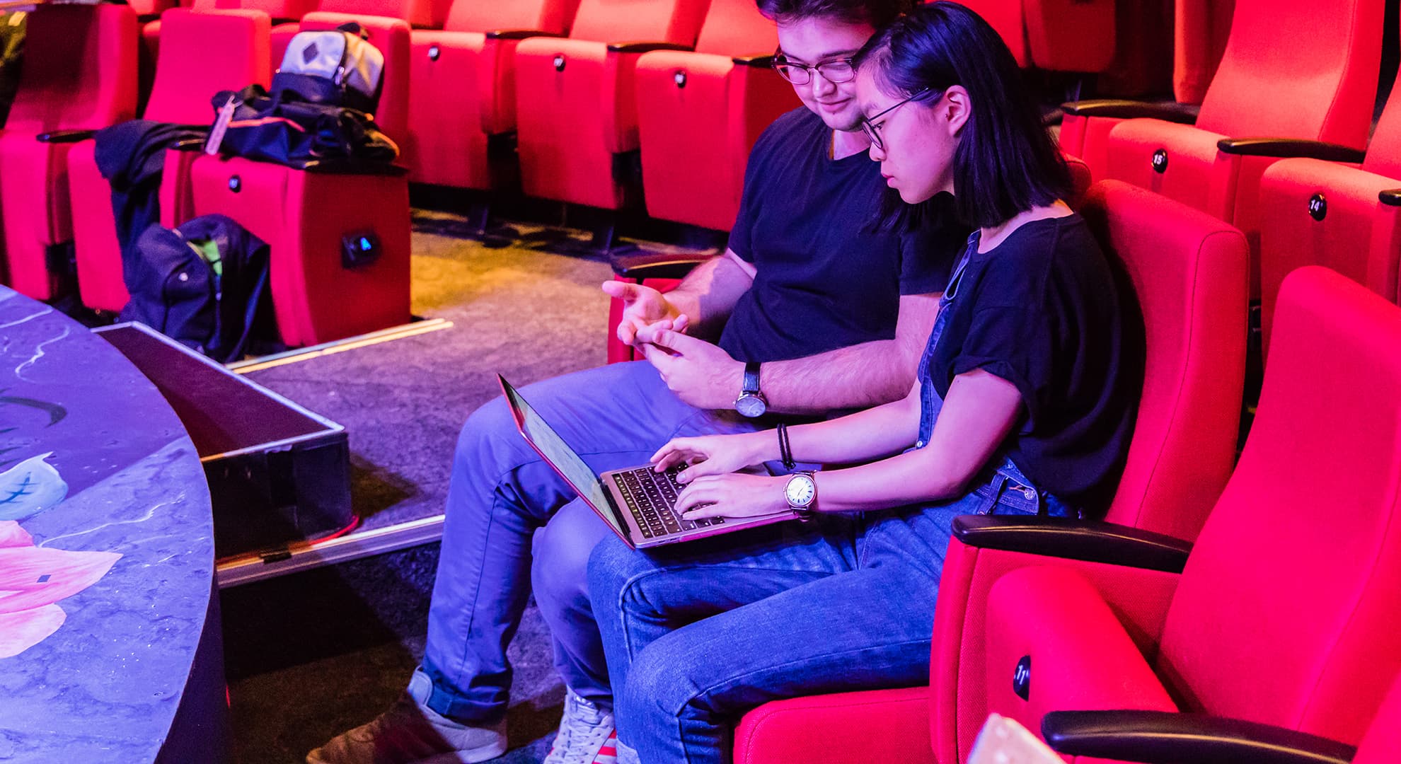 Two students in a performance space working on a laptop computer.