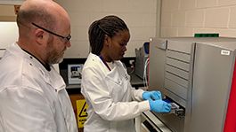 Image of a professor and research assistant in white lab coat inserting a slide into the gene titan machine