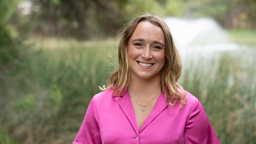 Bree Elliott grins and wears a bright pink blouse in front of the lake on the Joondalup Campus.