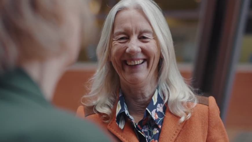 Head and shoulders of blonde woman with big smile in light orange suit jacket