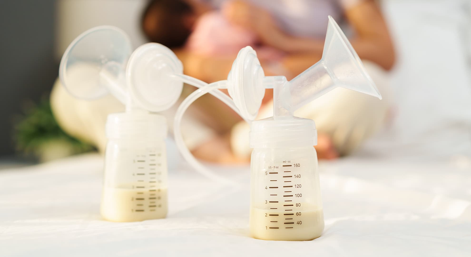 Two bottles of expressed milk, with mother and baby in the background