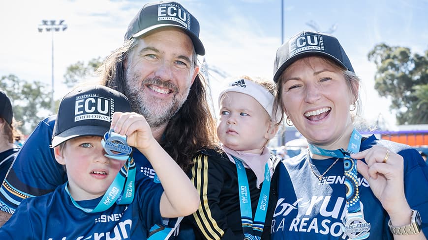 A family grins outdoors holding up their medals at the HBF Run for a Reason.