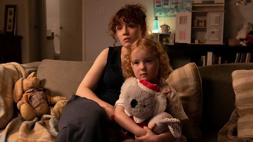 A mother and her daughter are sitting on the couch watching TV.