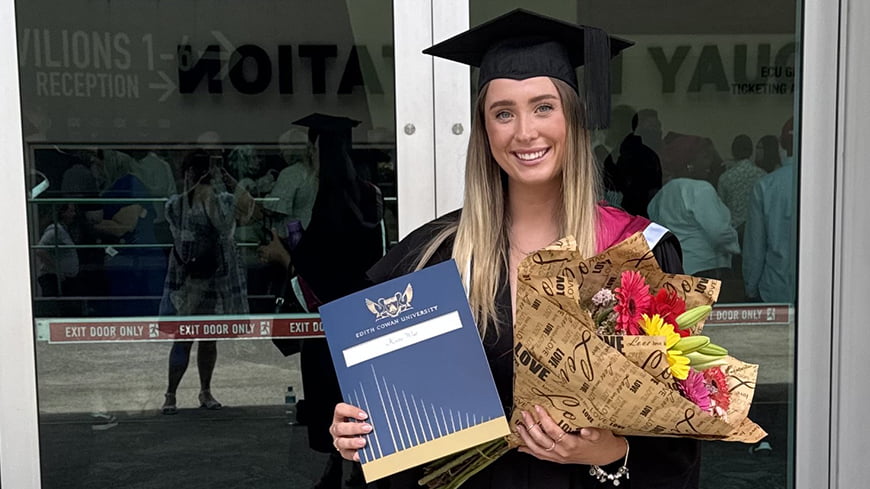 Person in graduation regalia holding bouquet of flowers.