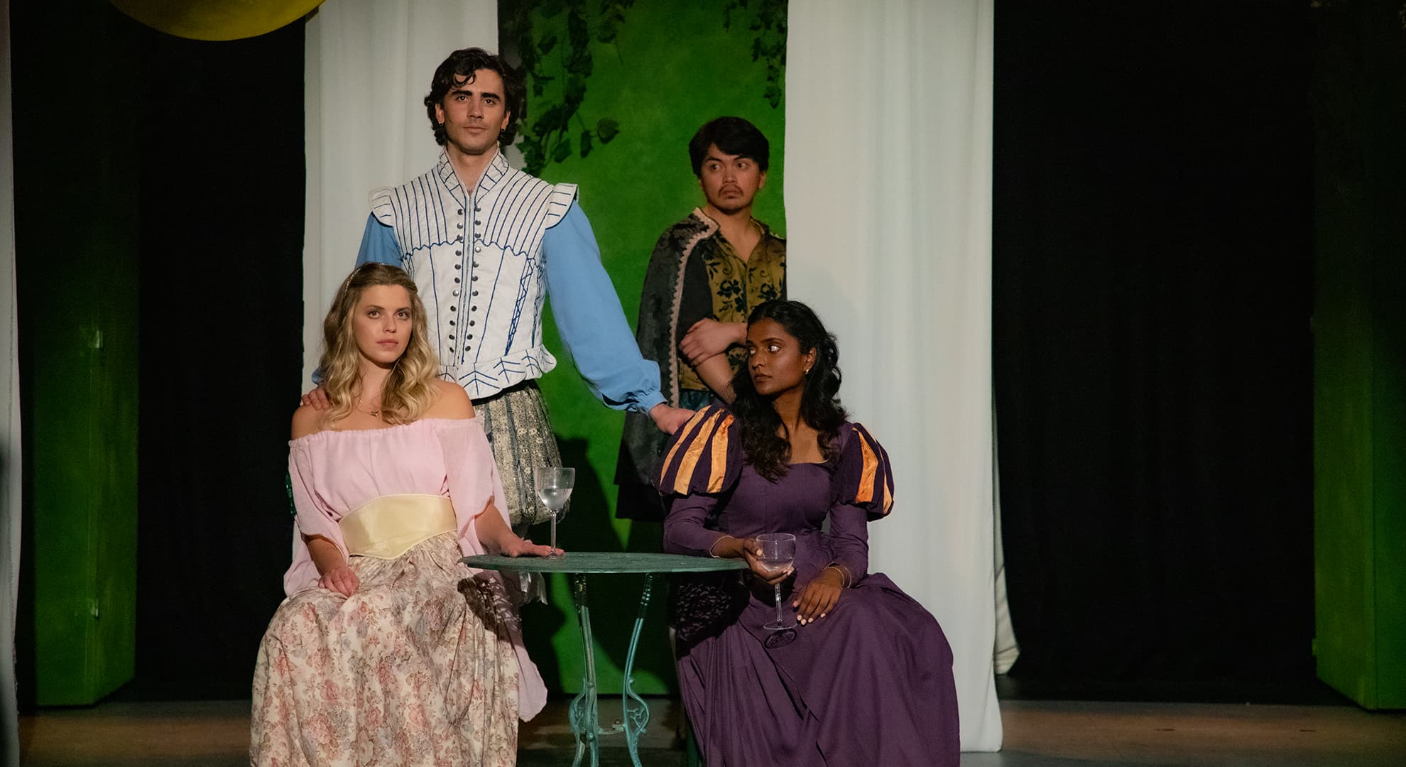 Four ECU students stand on stage dressed in dressed in theatre costumes.