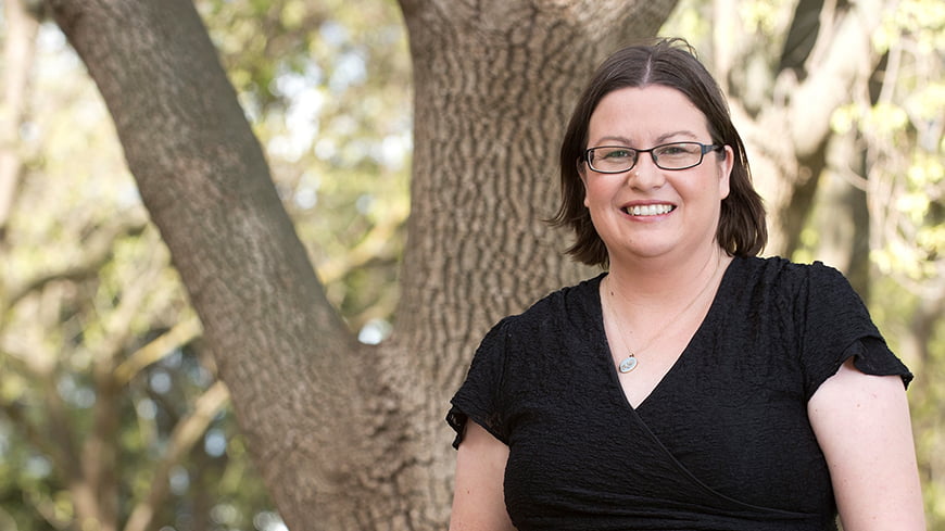 Smiling person standing in front of a tree outdoors.