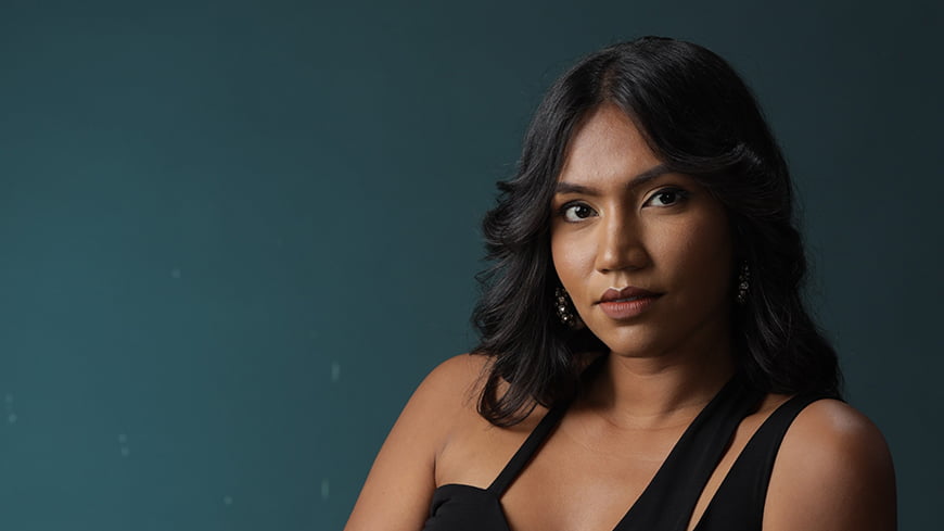 Person sitting in black dress against dark grey blue background.