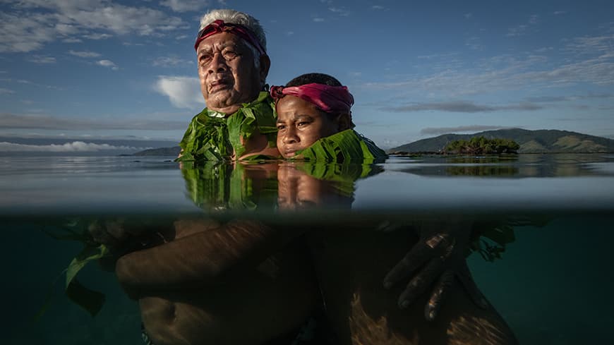 one of the elders on the remote Kioa Island in Fiji, Lotomau Fiafia was born in 1952 on the island and has lived his whole life there. He and his ten-year-old grandson John swim in the bay almost every day. In this photo they are standing where the shoreline used to be when Lotomau was young, but the sea level now is up to his chest.