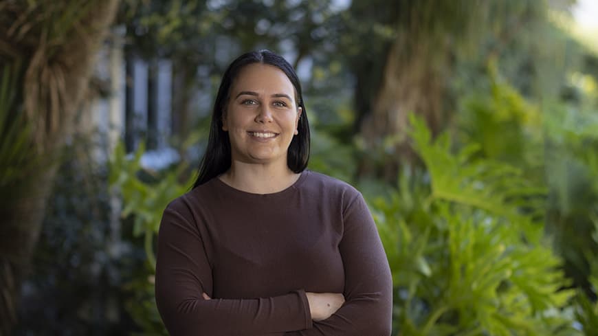 Smiling person in front of green ferns outdoors.