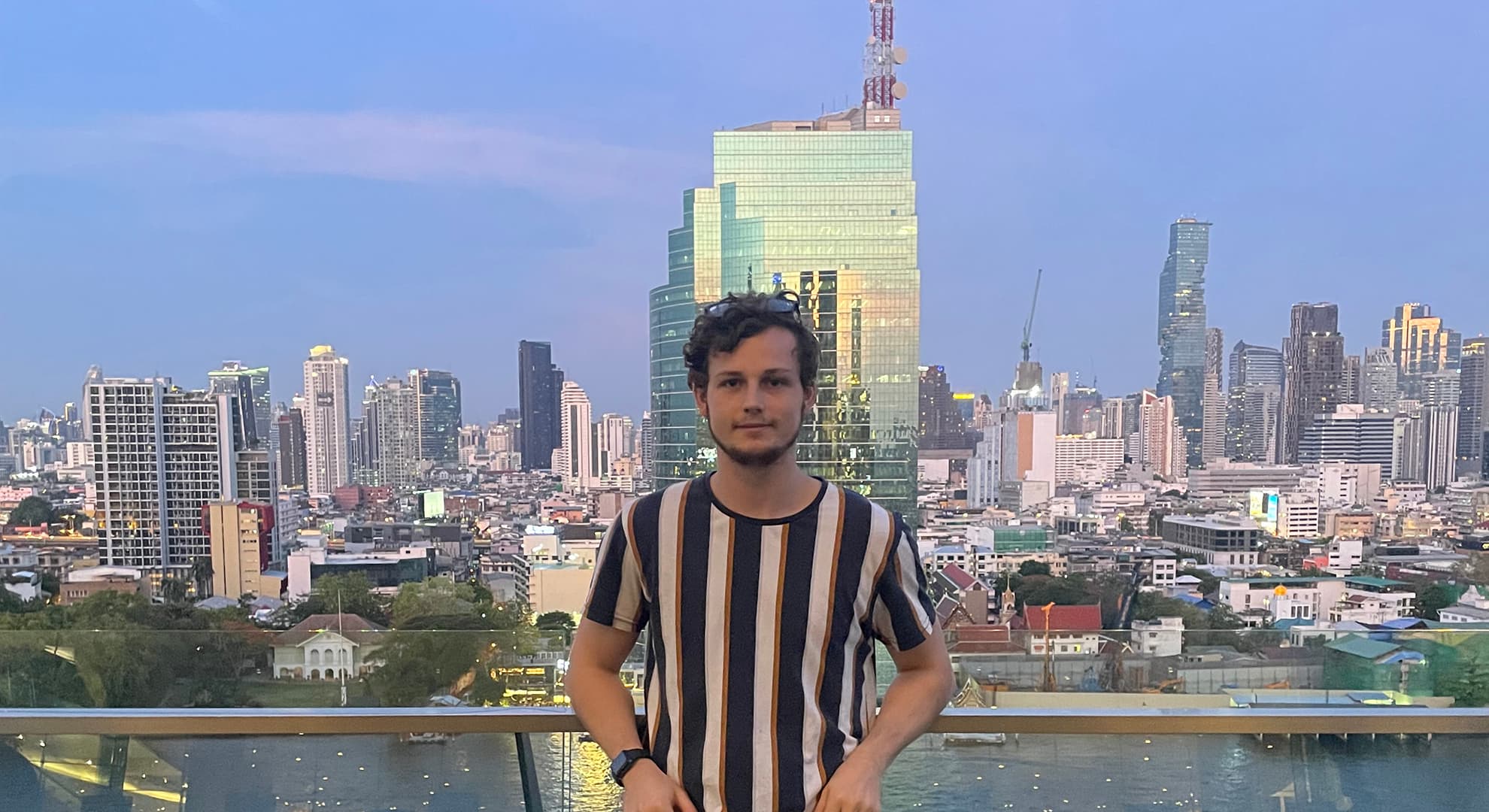 Ryan Bradley stands against glass railing with a dense city in the background.