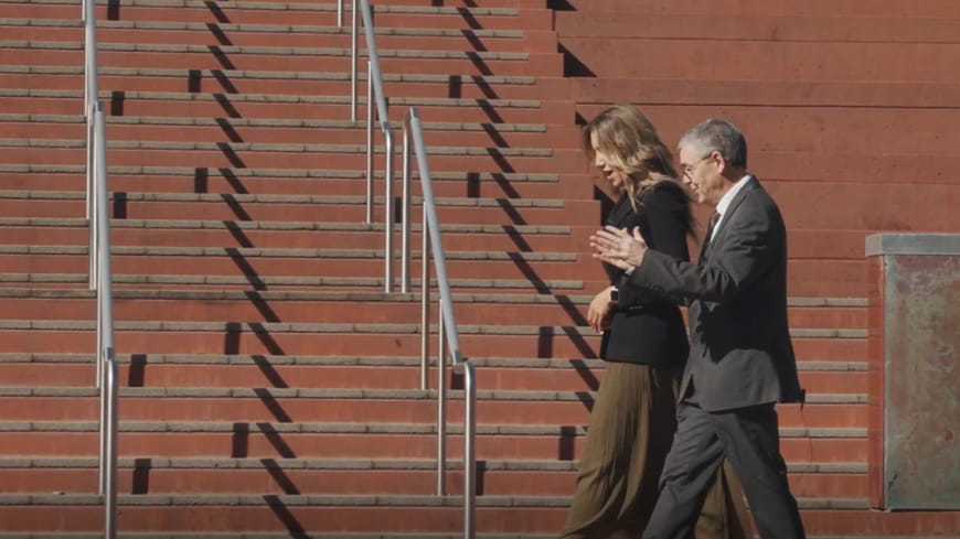 Profile of business woman and man talking as they stroll along in front of red bricks stars