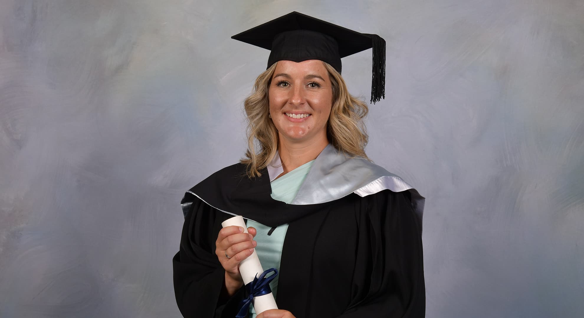 Person standing in front of grey background in graduation regalia