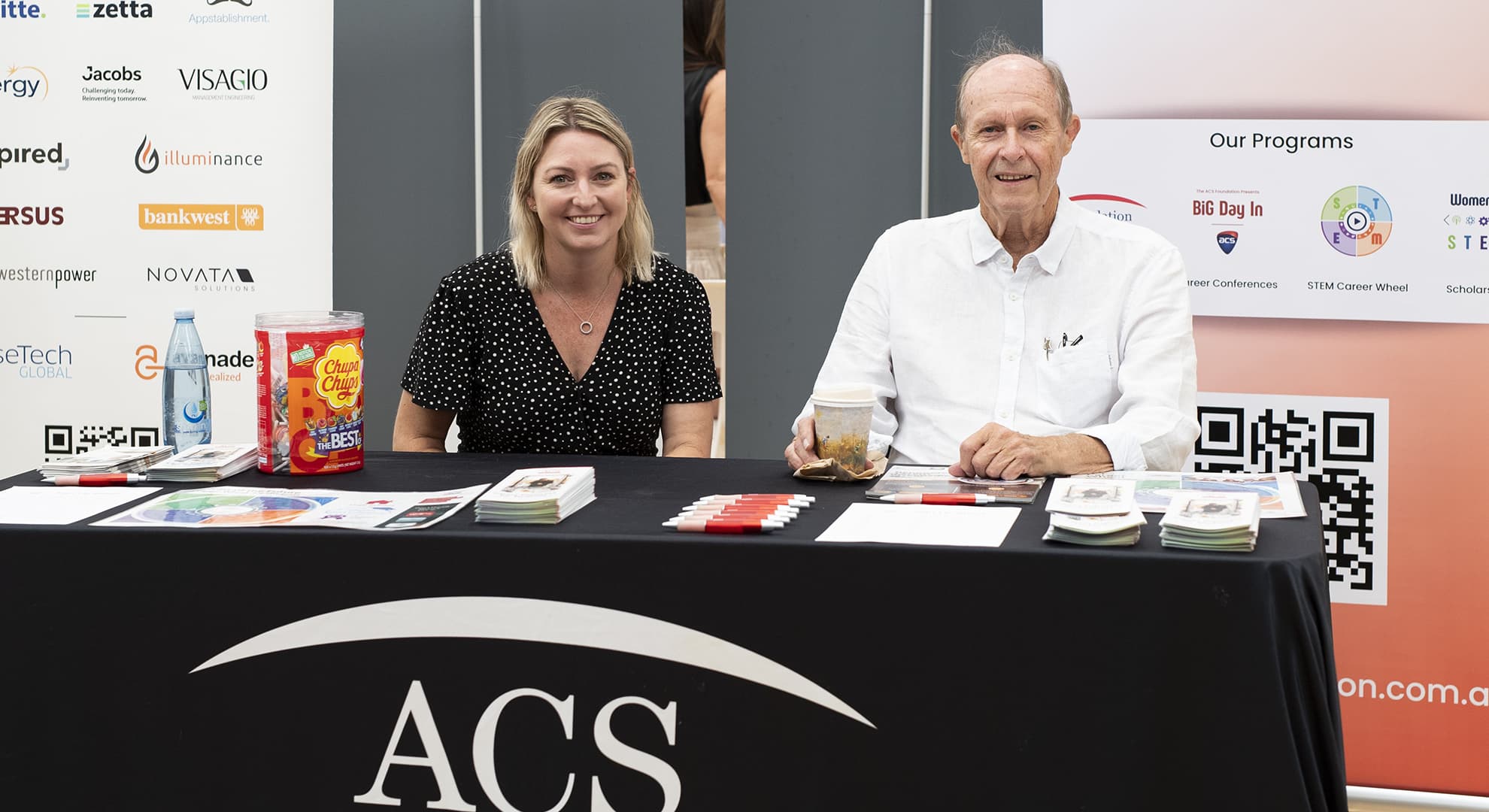 two people sitting behind a desk at a conference stand.