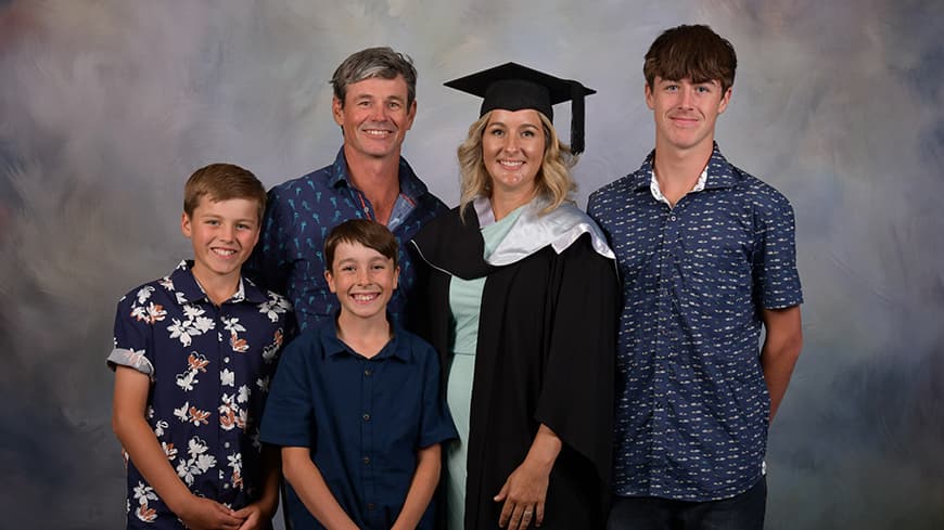 Family standing in front of grey background with one person in graduation regalia