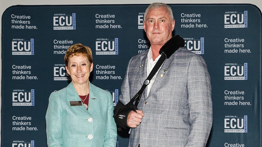 two smiling people in front of ECU branded wall.