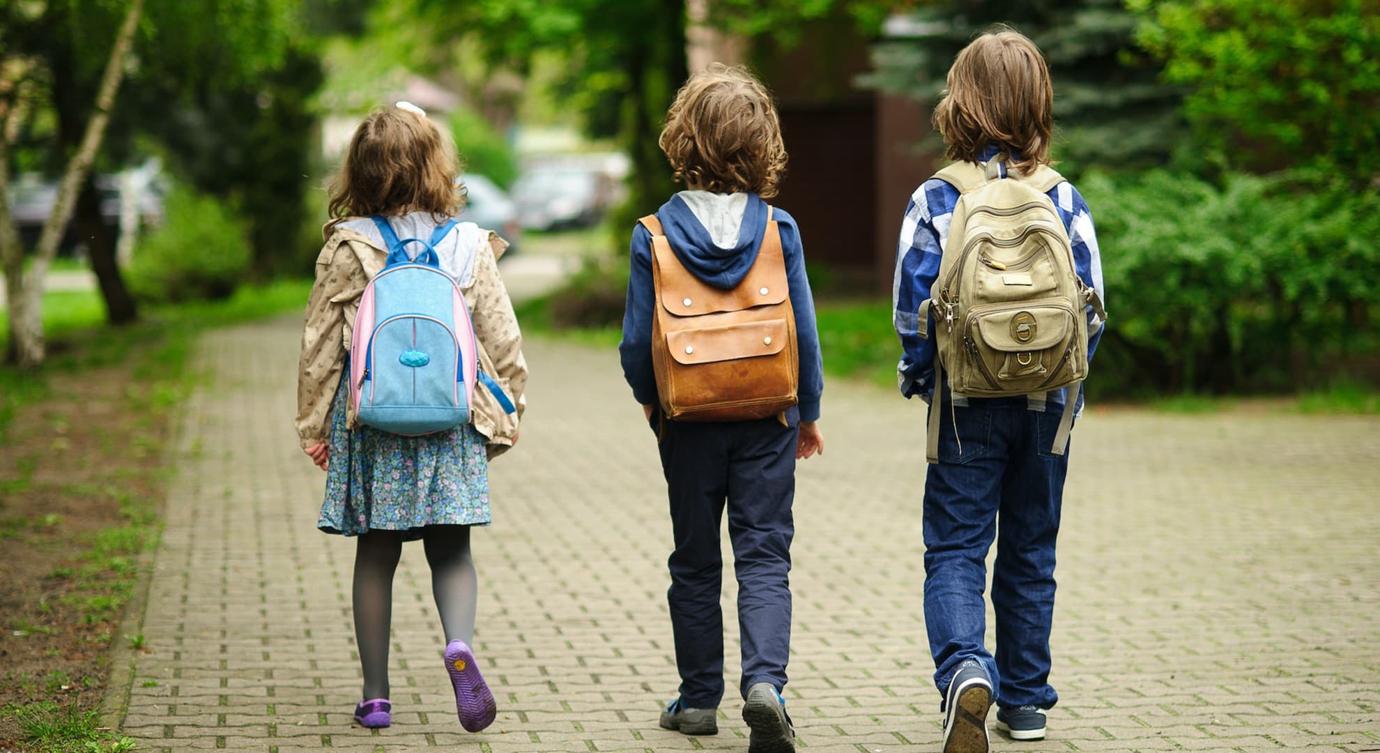 Three young children with backpacks walking away from the camera.